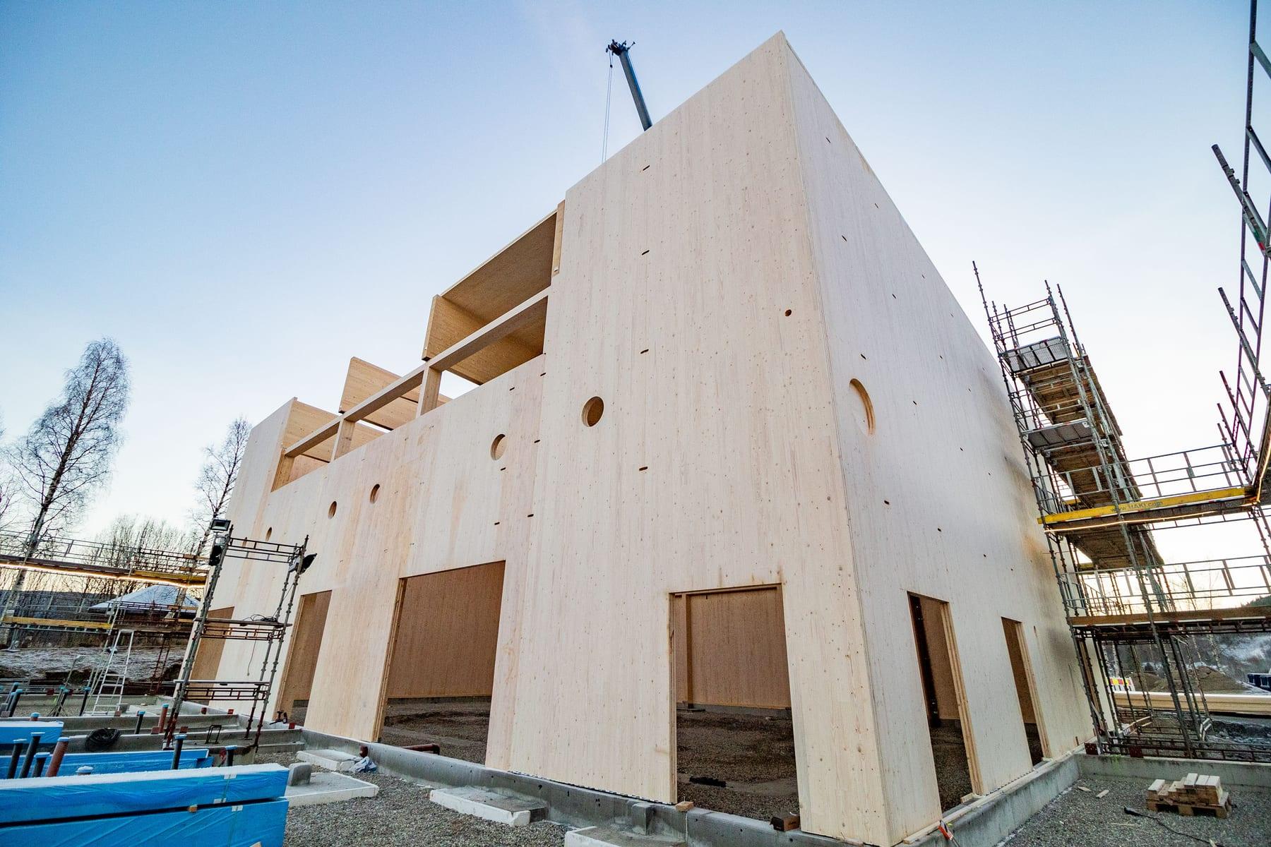 A solid timber building going up behind scaffolding, against a blue sky