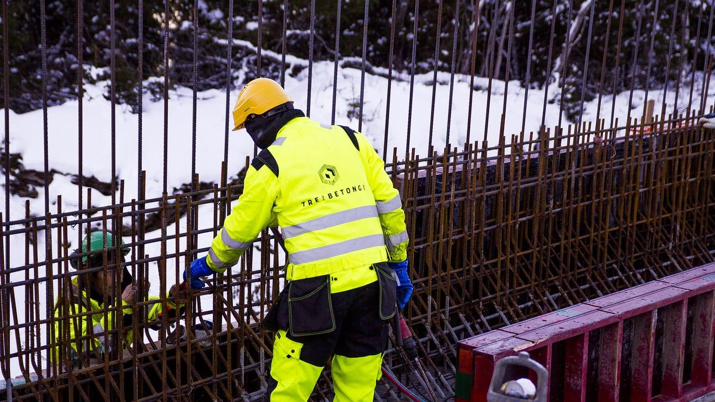 A worker in a hi-vis jacket with the Tre og Betong mark, working on reinforcement bars